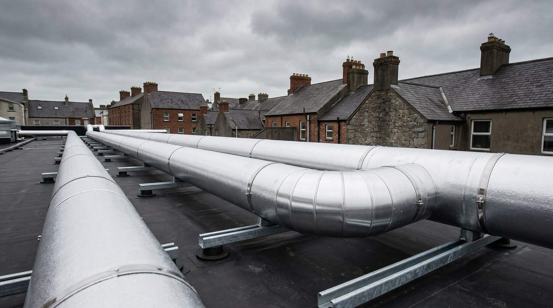 Aluminium-clad insulated pipework running across a commercial building rooftop under overcast sky